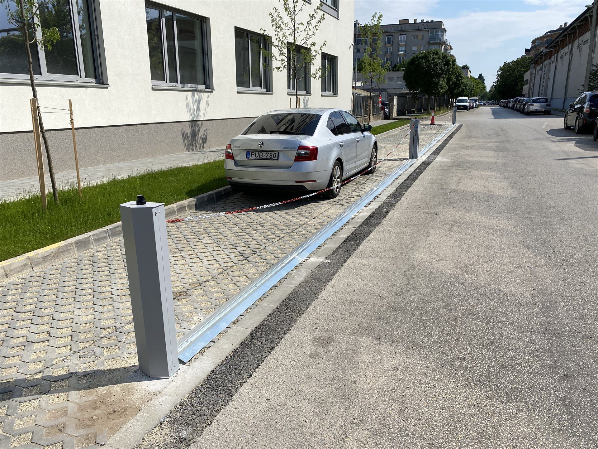 Kettenabsenker sperrt mit gespannter Kette eine ganze Stellplatzreihe vor einem Gebäude